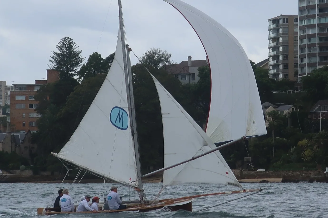 The replica Myra Too racing under spinnaker, blue oval M insignia on the mainsail
