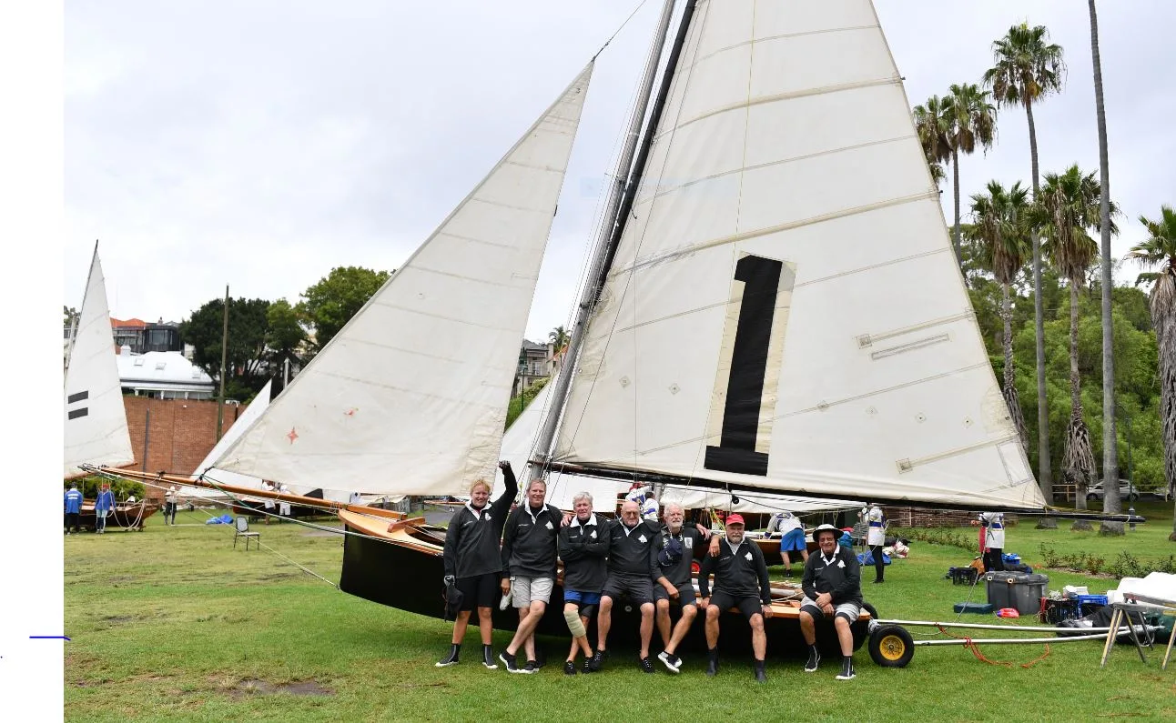 The replica Top Weight rigged on the clubhouse lawn, her crew lined along the hull beneath the black number 1 insignia on the mainsail