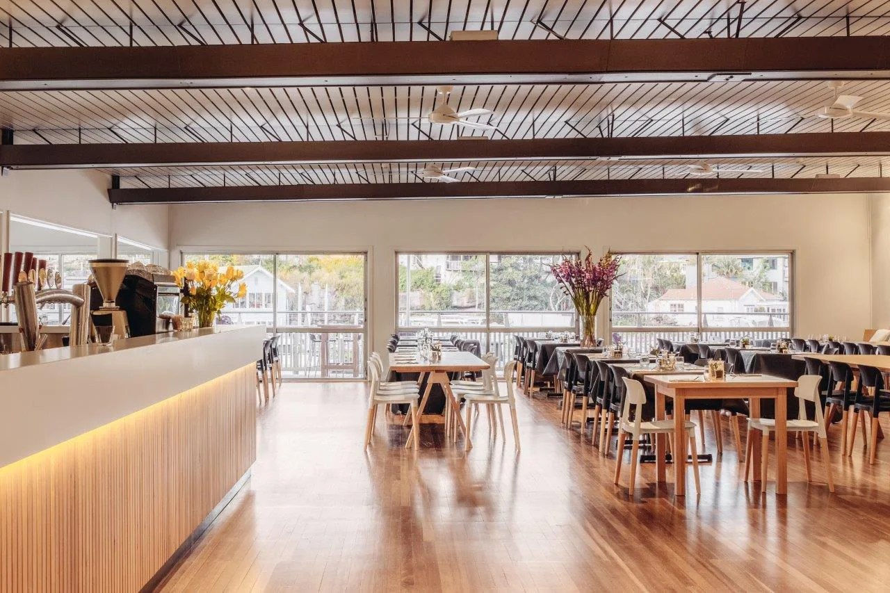 The clubhouse dining room with warm timber floors, an under-lit bar, fresh flowers and windows onto the water