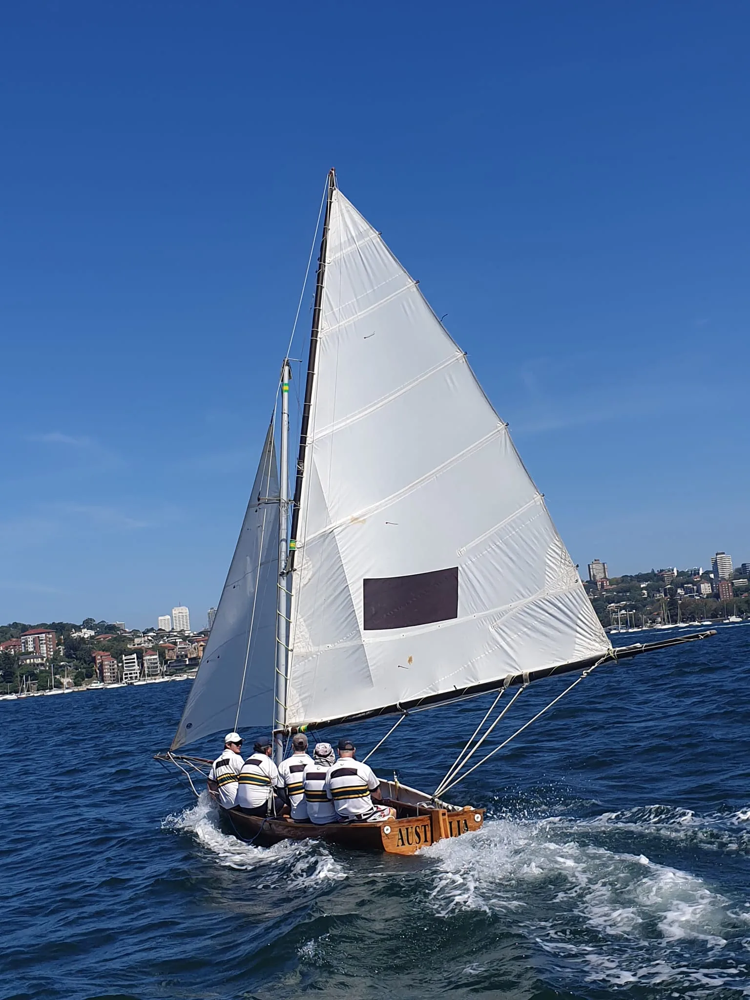 The replica Australia from astern under full sail, the black rectangle insignia on her mainsail and her name across the transom